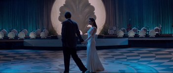 Movie still from “The Rocketeer” (1991), directed by Joe Johnston – A man and a woman holding hands in front of a fountain; Wide shot, Low angle