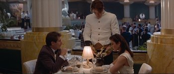 Movie still from “The Rocketeer” (1991), directed by Joe Johnston – A man standing at a table with two women; Medium shot, Over the shoulder angle