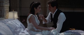 Movie still from “The Rocketeer” (1991), directed by Joe Johnston – A man and a woman sitting on a bed holding a wine glass; Medium shot, High angle