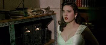 Movie still from “The Rocketeer” (1991), directed by Joe Johnston – A woman in a white dress sitting in front of a fireplace; Close Up shot, High angle