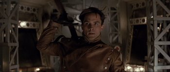 Movie still from “The Rocketeer” (1991), directed by Joe Johnston – A man in a brown leather jacket holding an arrow; Close Up shot, Low angle