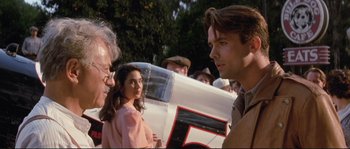 Movie still from “The Rocketeer” (1991), directed by Joe Johnston – A group of people standing next to each other near a car; Close Up shot, Over the shoulder angle