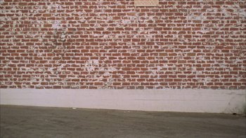 Movie still from “The Room” (2003), directed by Tommy Wiseau – A brick wall with a plaque on the side of it; Wide shot, Low angle