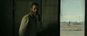 Movie still from “The Rover” (2014), directed by David Michôd – A man standing in front of a brick wall; Medium shot, Low angle