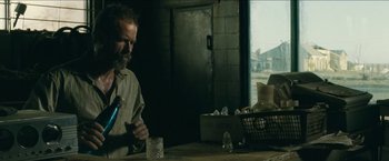 Movie still from “The Rover” (2014), directed by David Michôd – A man sitting at a table with a glass of water; Medium shot, Low angle