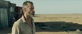 Movie still from “The Rover” (2014), directed by David Michôd – A man standing in a desert looking to his left; Close Up shot, Over the shoulder angle