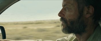 Movie still from “The Rover” (2014), directed by David Michôd – A man with a long beard is looking out a window; Close Up shot, Over the shoulder angle