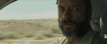 Movie still from “The Rover” (2014), directed by David Michôd – A person with a beard looking at the camera; Close Up shot, Over the shoulder angle