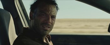 Movie still from “The Rover” (2014), directed by David Michôd – A person in a car on a road; Close Up shot, Over the shoulder angle