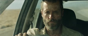Movie still from “The Rover” (2014), directed by David Michôd – A person with a beard driving a car; Close Up shot, Over the shoulder angle