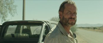 Movie still from “The Rover” (2014), directed by David Michôd – A person standing next to a truck; Close Up shot, Over the shoulder angle