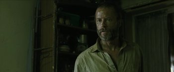 Movie still from “The Rover” (2014), directed by David Michôd – A man with a goatee standing in front of shelves; Close Up shot, Low angle