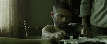 Movie still from “The Rover” (2014), directed by David Michôd – A man sitting at a table with a knife in his hand; Close Up shot, Over the shoulder angle