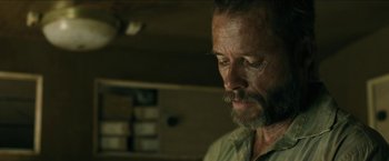 Movie still from “The Rover” (2014), directed by David Michôd – A person with a beard looking down; Close Up shot, Over the shoulder angle