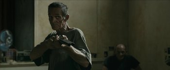 Movie still from “The Rover” (2014), directed by David Michôd – An older man holding a gun while standing next to another man; Medium shot, Over the shoulder angle