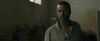 Movie still from “The Rover” (2014), directed by David Michôd – A man with a goatee is standing in a room; Close Up shot, Over the shoulder angle