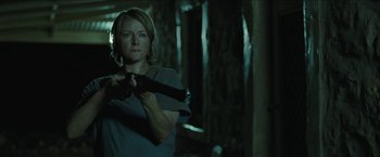 Movie still from “The Rover” (2014), directed by David Michôd – A woman is holding a gun in a dark room; Medium shot, Low angle