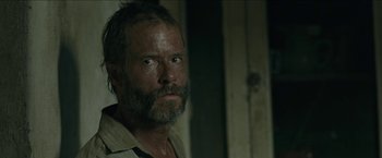 Movie still from “The Rover” (2014), directed by David Michôd – A person with a beard looking at the camera; Close Up shot, Over the shoulder angle