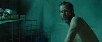 Movie still from “The Rover” (2014), directed by David Michôd – A man with a beard is standing in the water; Close Up shot, Low angle