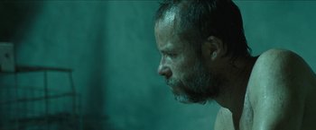 Movie still from “The Rover” (2014), directed by David Michôd – A person's face in a room; Close Up shot, Over the shoulder angle