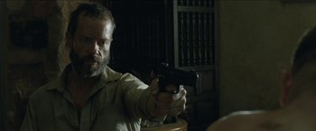 Movie still from “The Rover” (2014), directed by David Michôd – A man holding a gun in a room; Close Up shot, Over the shoulder angle