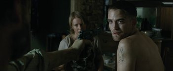 Movie still from “The Rover” (2014), directed by David Michôd – A man holding a gun in front of a woman in a room; Medium shot, Over the shoulder angle