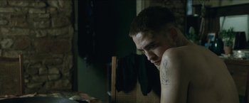 Movie still from “The Rover” (2014), directed by David Michôd – A man with a tattoo on his arm sitting in a room; Close Up shot, High angle