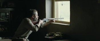 Movie still from “The Rover” (2014), directed by David Michôd – A man holding a gun in front of a window; Medium shot, Low angle