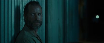 Movie still from “The Rover” (2014), directed by David Michôd – A man with a beard is standing in a room; Close Up shot, Over the shoulder angle