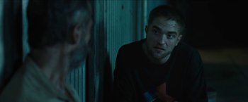 Movie still from “The Rover” (2014), directed by David Michôd – A person sitting in front of a wall; Medium shot, Over the shoulder angle