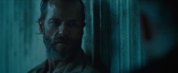 Movie still from “The Rover” (2014), directed by David Michôd – A person with a beard looking at the camera; Close Up shot, Low angle