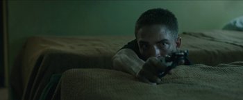 Movie still from “The Rover” (2014), directed by David Michôd – A man laying on a bed holding a remote control; Medium shot, High angle