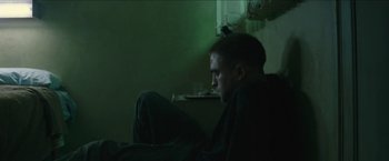 Movie still from “The Rover” (2014), directed by David Michôd – A man sitting on a couch in a dark room; Medium shot, Low angle