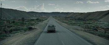 Movie still from “The Rover” (2014), directed by David Michôd – A car driving down the middle of a road; Extreme Wide shot, High angle