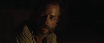 Movie still from “The Rover” (2014), directed by David Michôd – A person with a beard looking at the camera; Close Up shot, Over the shoulder angle