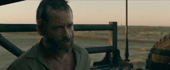 Movie still from “The Rover” (2014), directed by David Michôd – A man with a beard is sitting in the desert; Close Up shot, Over the shoulder angle