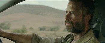 Movie still from “The Rover” (2014), directed by David Michôd – A person looking out a window; Close Up shot, Over the shoulder angle