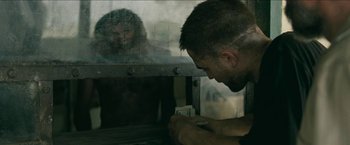 Movie still from “The Rover” (2014), directed by David Michôd – A man looking at a card in front of a window; Medium shot, Over the shoulder angle
