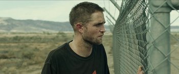 Movie still from “The Rover” (2014), directed by David Michôd – A person near a chain link fence; Close Up shot, Over the shoulder angle