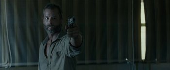 Movie still from “The Rover” (2014), directed by David Michôd – A man is holding a gun in a room; Close Up shot, Over the shoulder angle
