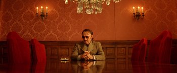 Movie still from “The Royal Tenenbaums” (2001), directed by Wes Anderson – An older man sitting at a table in front of a chandelier; Medium shot, Low angle