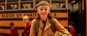 Movie still from “The Royal Tenenbaums” (2001), directed by Wes Anderson – A young boy wearing a head band standing in front of a school bus; Close Up shot, Over the shoulder angle