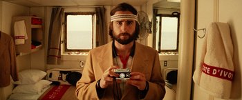 Movie still from “The Royal Tenenbaums” (2001), directed by Wes Anderson – A man holding a camera in a room with a fan; Medium shot, Low angle