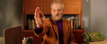 Movie still from “The Royal Tenenbaums” (2001), directed by Wes Anderson – An older man in a brown jacket is holding his hands up; Medium shot, Over the shoulder angle
