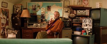 Movie still from “The Royal Tenenbaums” (2001), directed by Wes Anderson – An older man sitting in a chair in front of a map; Medium shot, Over the shoulder angle