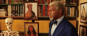 Movie still from “The Royal Tenenbaums” (2001), directed by Wes Anderson – An older man standing in front of two native american paintings; Close Up shot, Low angle