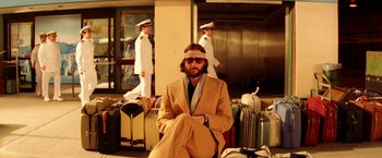 Movie still from “The Royal Tenenbaums” (2001), directed by Wes Anderson – A man sitting on the ground in front of suitcases; Medium shot, Low angle