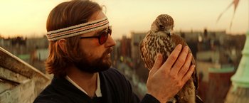 Movie still from “The Royal Tenenbaums” (2001), directed by Wes Anderson – A man holding a bird in his hand while standing next to a building; Close Up shot, Low angle