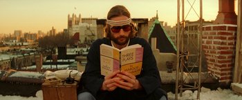 Movie still from “The Royal Tenenbaums” (2001), directed by Wes Anderson – A man reading a three plays book on a ledge; Close Up shot, Low angle