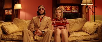 Movie still from “The Royal Tenenbaums” (2001), directed by Wes Anderson – A man and a woman sitting on a yellow couch; Medium shot, Low angle